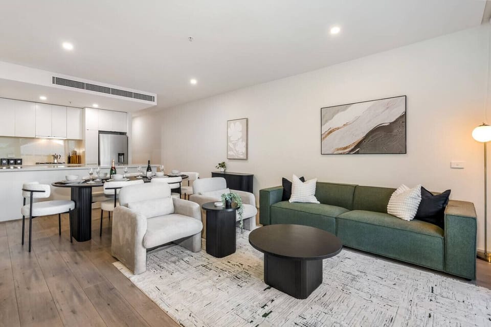 Bright open plan living and dining area with modern kitchen, plush seating, and stylish decor. Perfect for relaxing or hosting meals together, with warm lighting and a spacious, inviting layout.