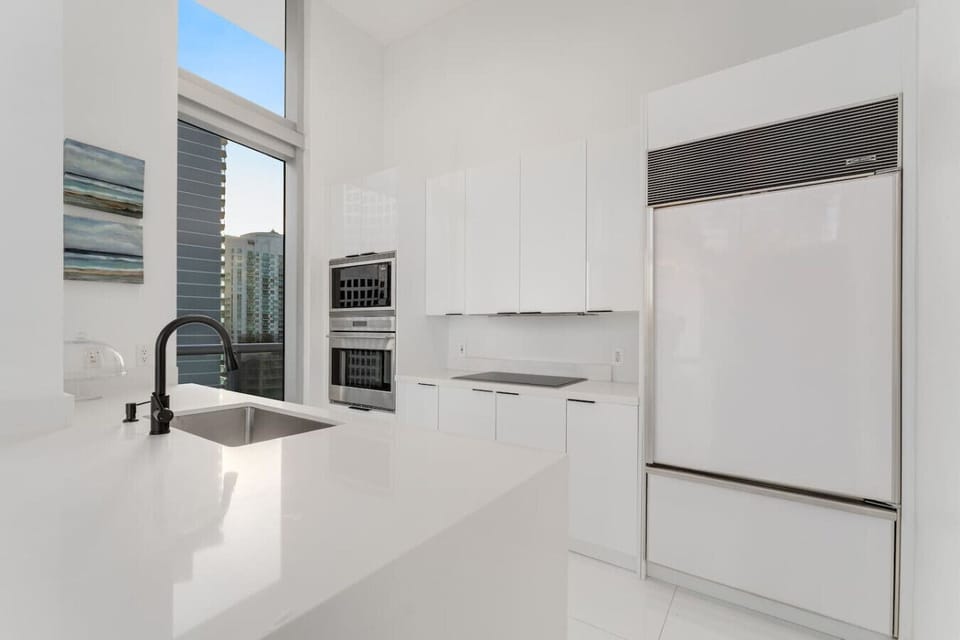 This sleek, modern kitchen features high-gloss cabinetry, a Sub-Zero fridge, built-in Bosch ovens, and minimalist black fixtures. Fully stocked with cookware, dinnerware, utensils, and glassware ready for anything from morning coffee to gourmet meals