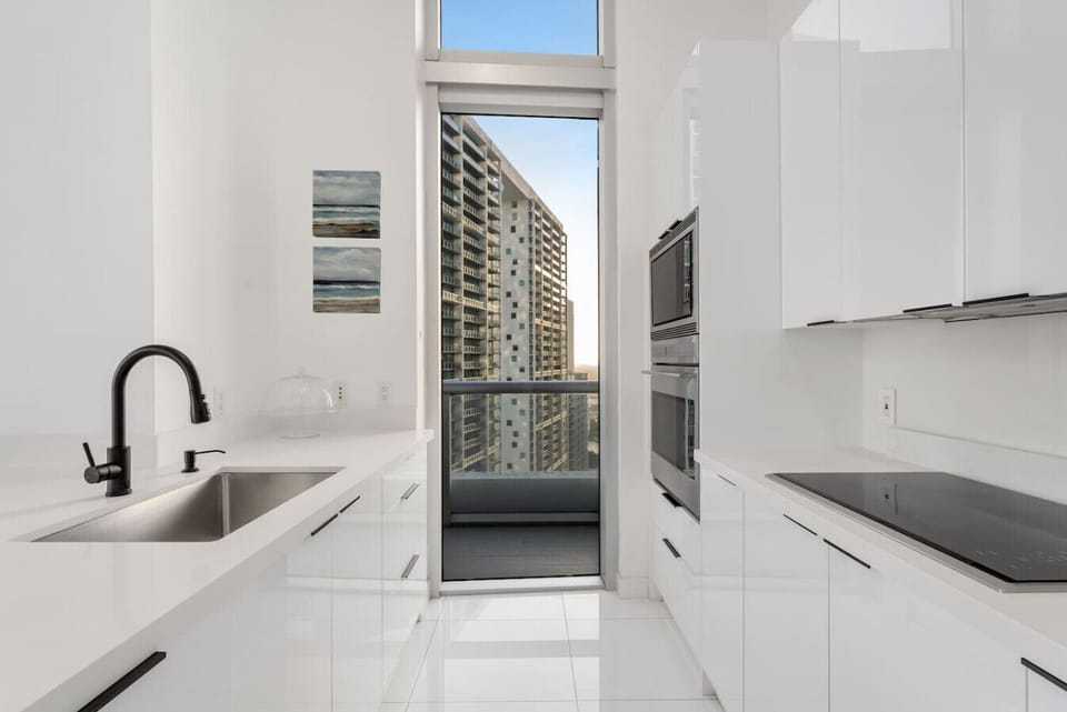 This sleek, modern kitchen features high-gloss cabinetry, a Sub-Zero fridge, built-in Bosch ovens, and minimalist black fixtures. Fully stocked with cookware, dinnerware, utensils, and glassware ready for anything from morning coffee to gourmet meals