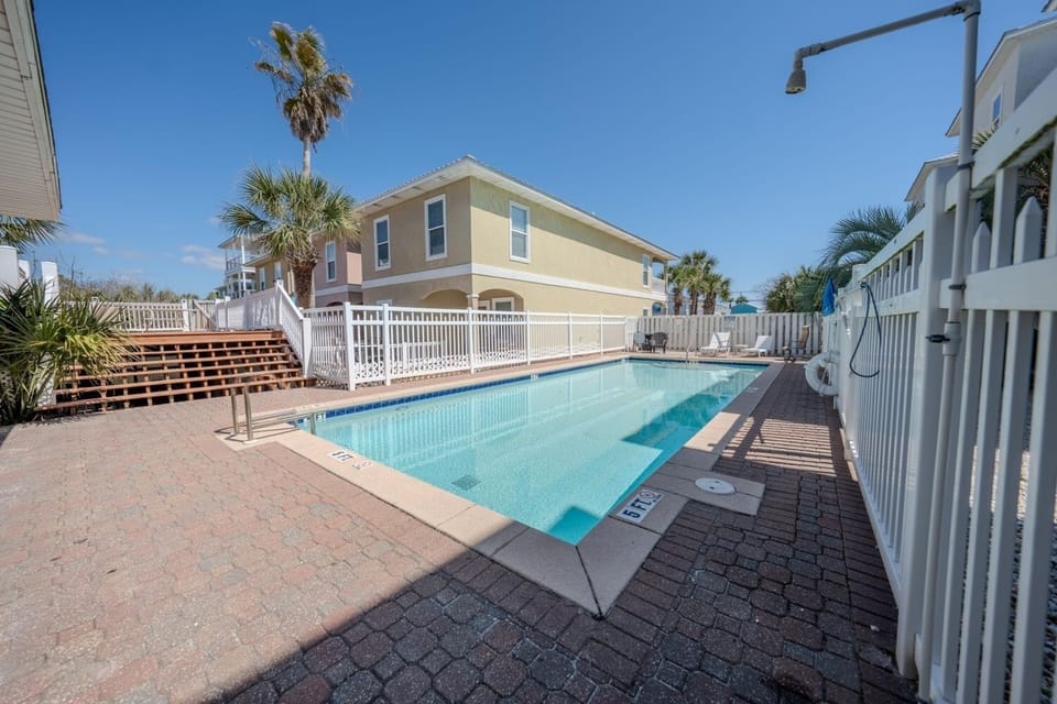 Coastal vacation rental community featuring swimming pool surrounded by tropical palms and colorful beach houses.