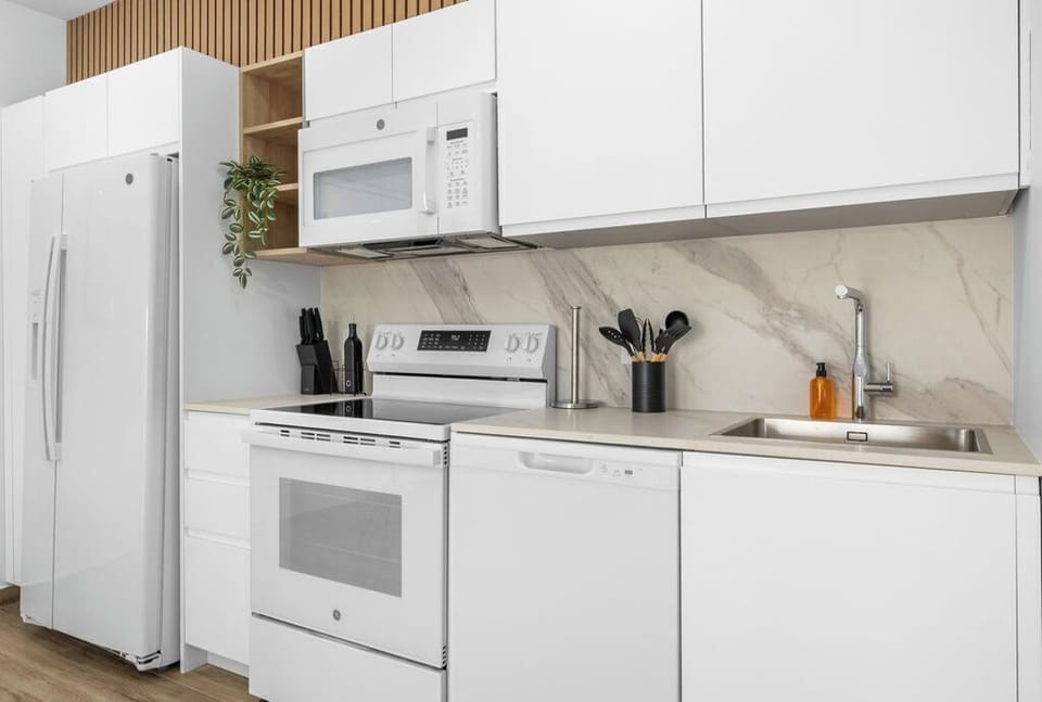 Bright white-toned kitchen equipped with a microwave, stove, oven, and all essential utensils provided.