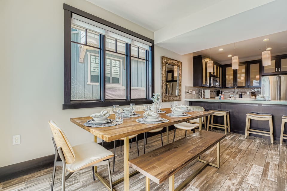 Gather around this inviting dining table where your group can share meals, laughter, and memories. Natural light pours through large windows, while the sleek kitchen waits nearby for your culinary adventures.
