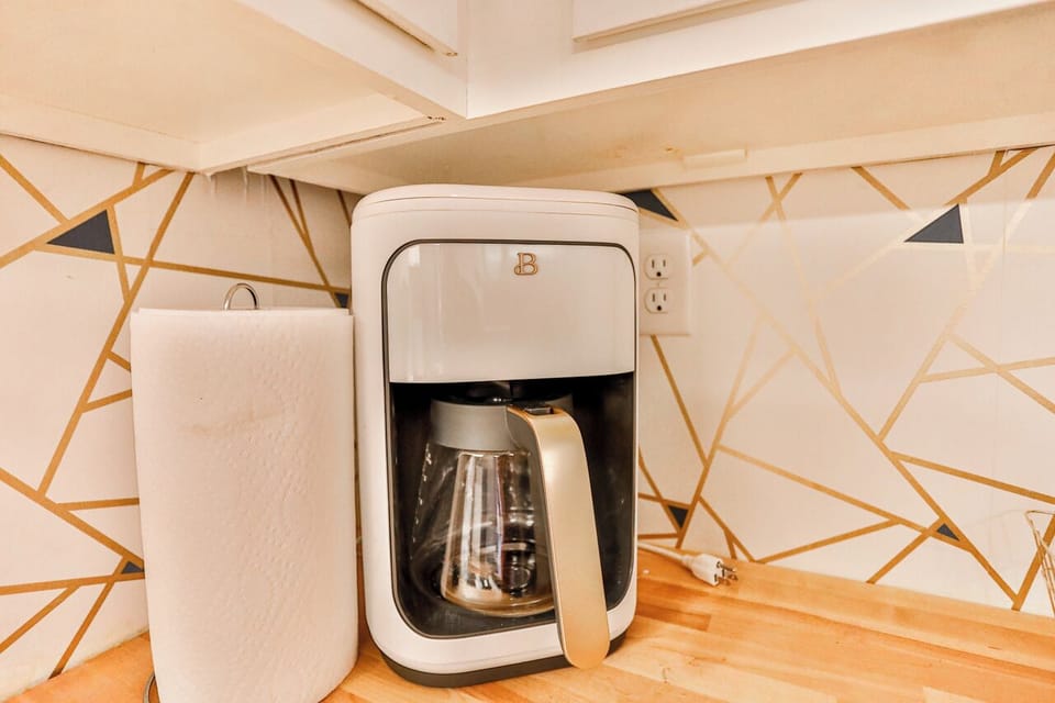 A modern kitchen equipped with high-end appliances and ample lighting. It has a coffee maker, oven, stove top, utensils, and all it takes to fix a delicious meal.