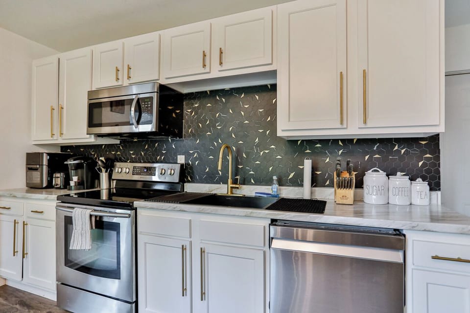 A modern kitchen equipped with high-end appliances and ample lighting. It has a coffee maker, oven, stove top, utensils, and all it takes to fix a delicious meal.