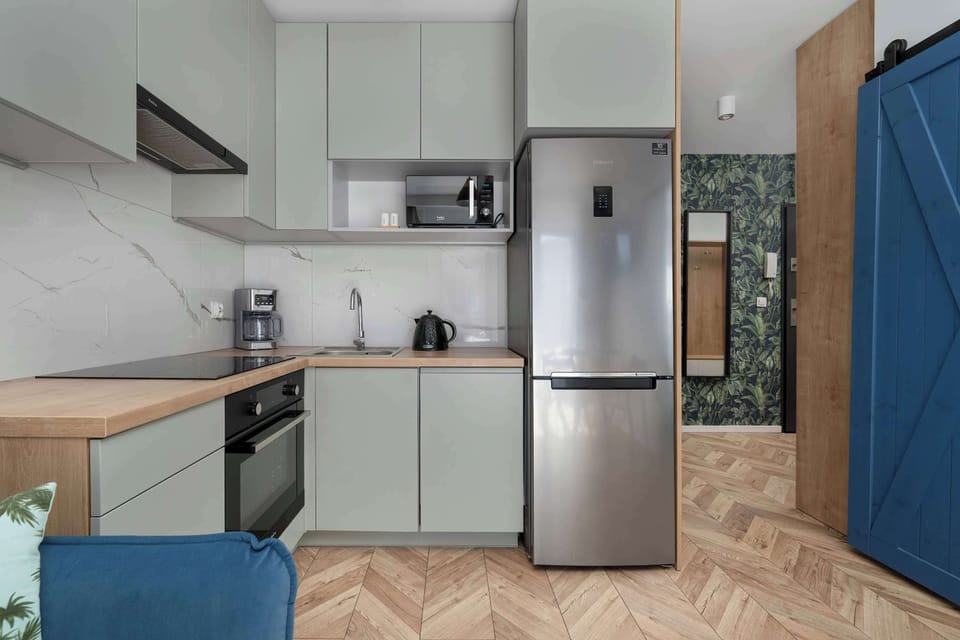 Modern kitchen with white cabinets, wooden countertop, and practical appliances including oven, fridge, kettle, and coffee machine.