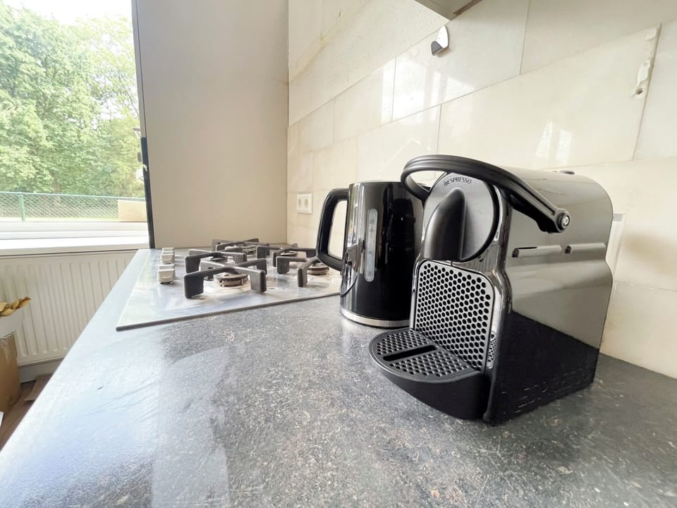 Modern kitchen setup with a coffee machine, kettle, and gas stove on a sleek black countertop.

