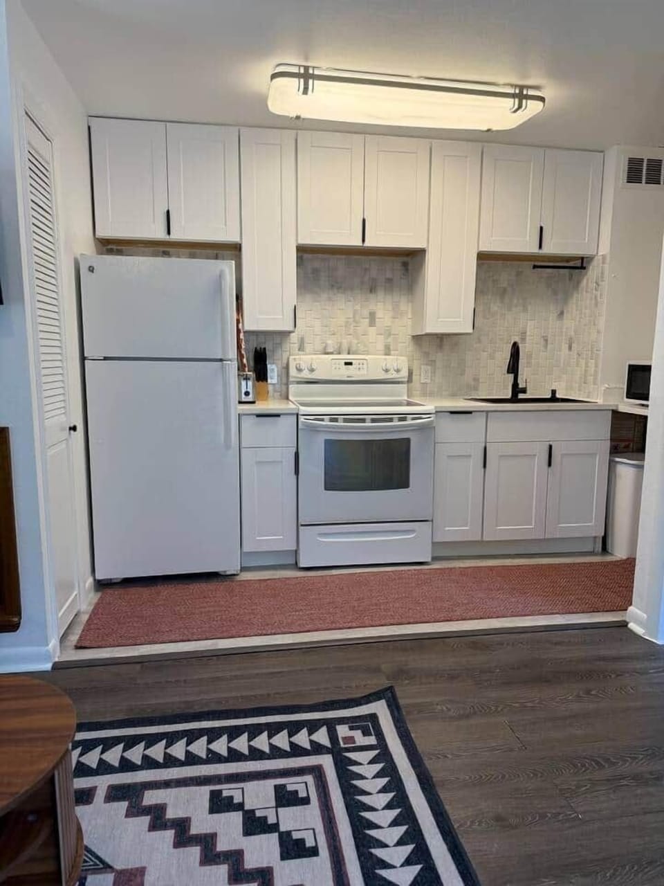 This bright kitchen is cooking up style and function. With fresh white cabinets, a bold backsplash, and all the essentials, it’s the perfect spot to whip up breakfast or heat leftovers. The red rug adds just the right pop of cozy.