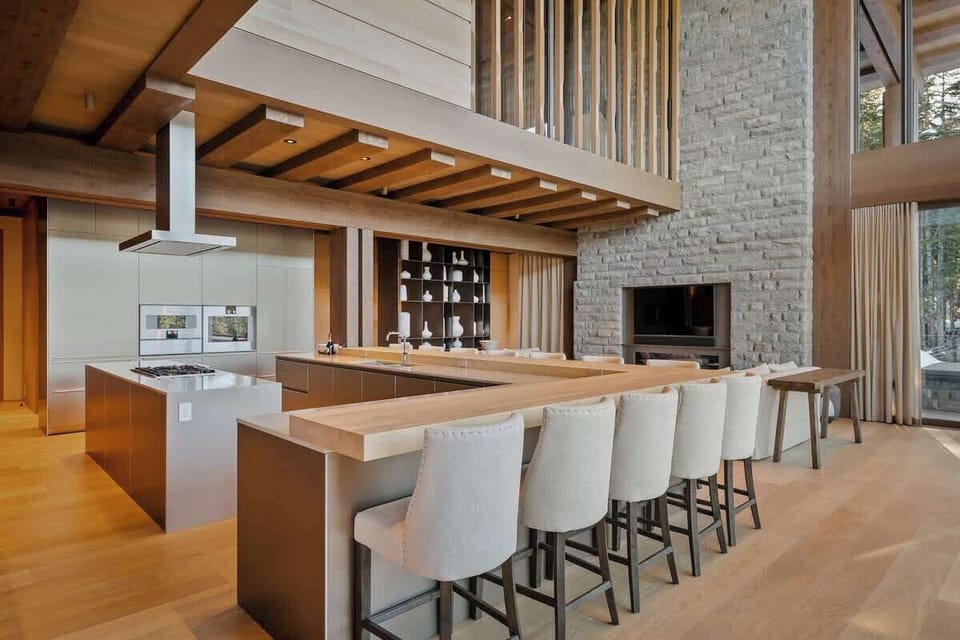 - Open kitchen and lounge area with elegant mountain-style decor  
- Stone fireplace and high ceilings create a warm cozy setting  
- Perfect blend of rustic textures and modern alpine design  
