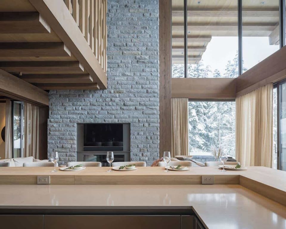 - Sleek breakfast bar setup beside tall glass walls and fireplace  
- Stylish dining setting with panoramic forest and slope backdrop  
- Enjoy warm meals while snow falls gently outside  