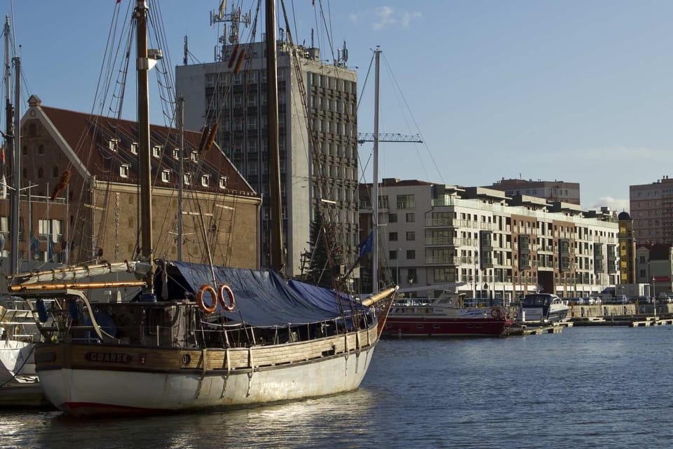 A stunning outdoor shot of a waterfront area, featuring a traditional sailing ship moored by the quay. Historic brick buildings line the background, showcasing charming architecture.