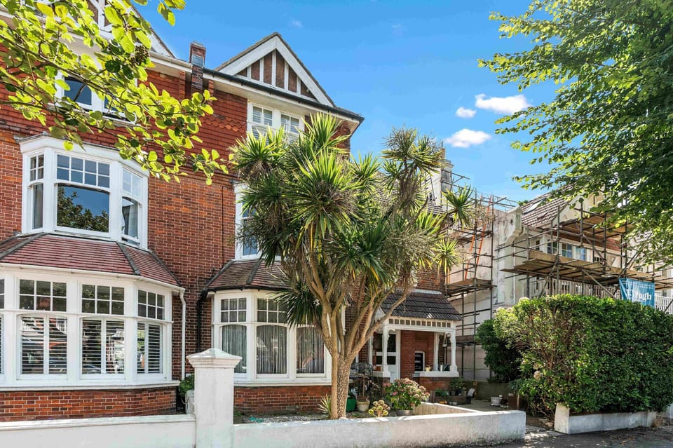 Exterior view of Hove Sunrise Apartment, a charming top-floor home within a traditional Hove townhouse. The building features classic brickwork, large sash windows, and a welcoming entrance, perfectly situated near the seafront.