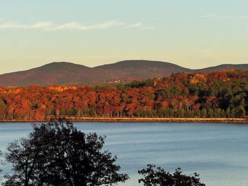 A stunning autumn landscape with vibrant fall foliage covering rolling hills beside a peaceful lake.