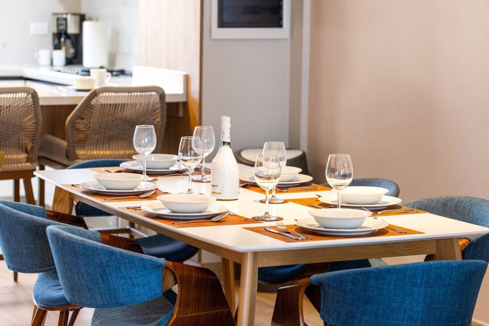 Dining table with elegant glassware, a wine bottle, and neatly arranged plates and utensils. Chairs with woven backs complete the modern dining area.