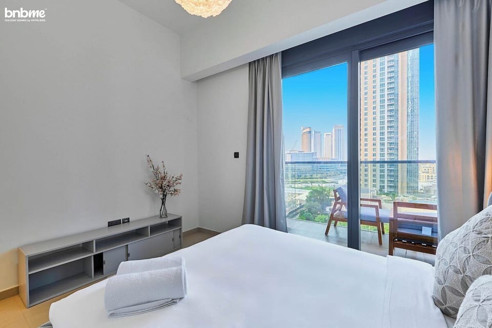 Relax in the stylish second bedroom featuring a plush queen-size bed, chic décor, and balcony access with stunning Downtown Dubai skyline views—perfect for sunset lounging.