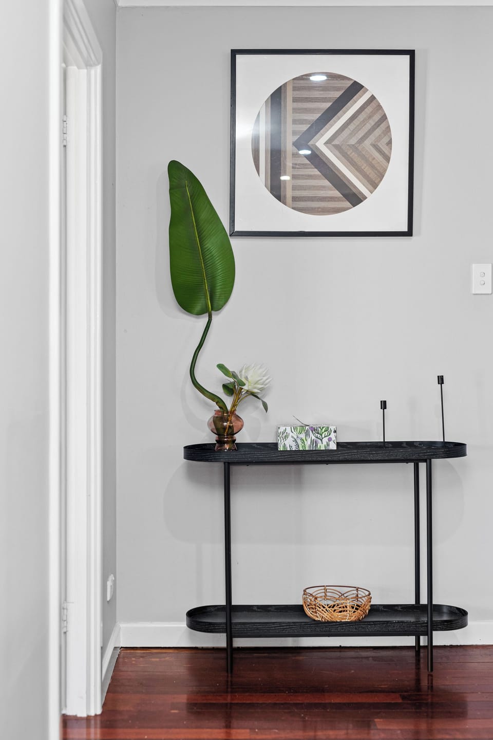 A chic entryway console with modern decor, including a unique large leaf and abstract artwork.