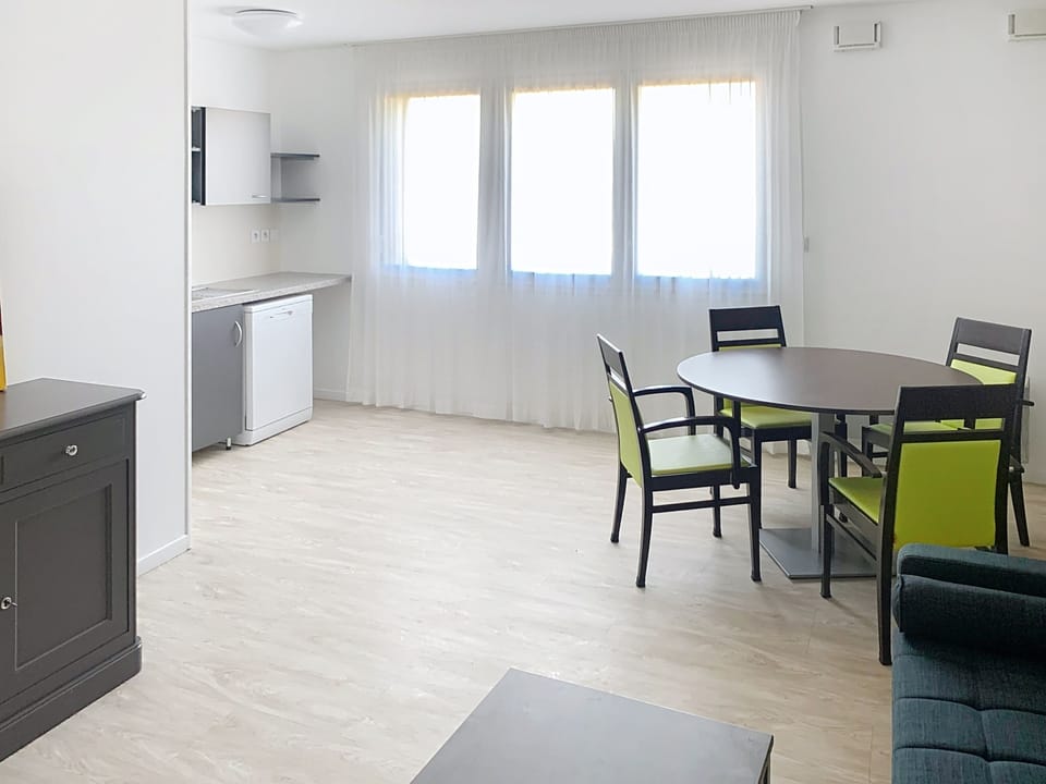 Open plan living and dining space with green accent chairs and ample natural light.