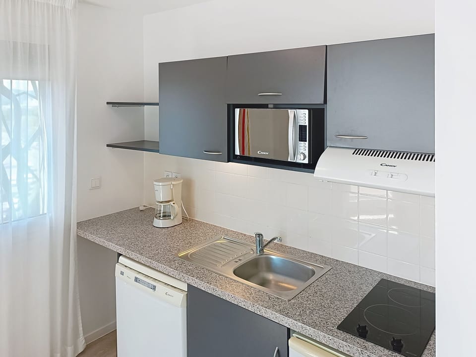 Kitchen with sink, appliances, and window with curtains.