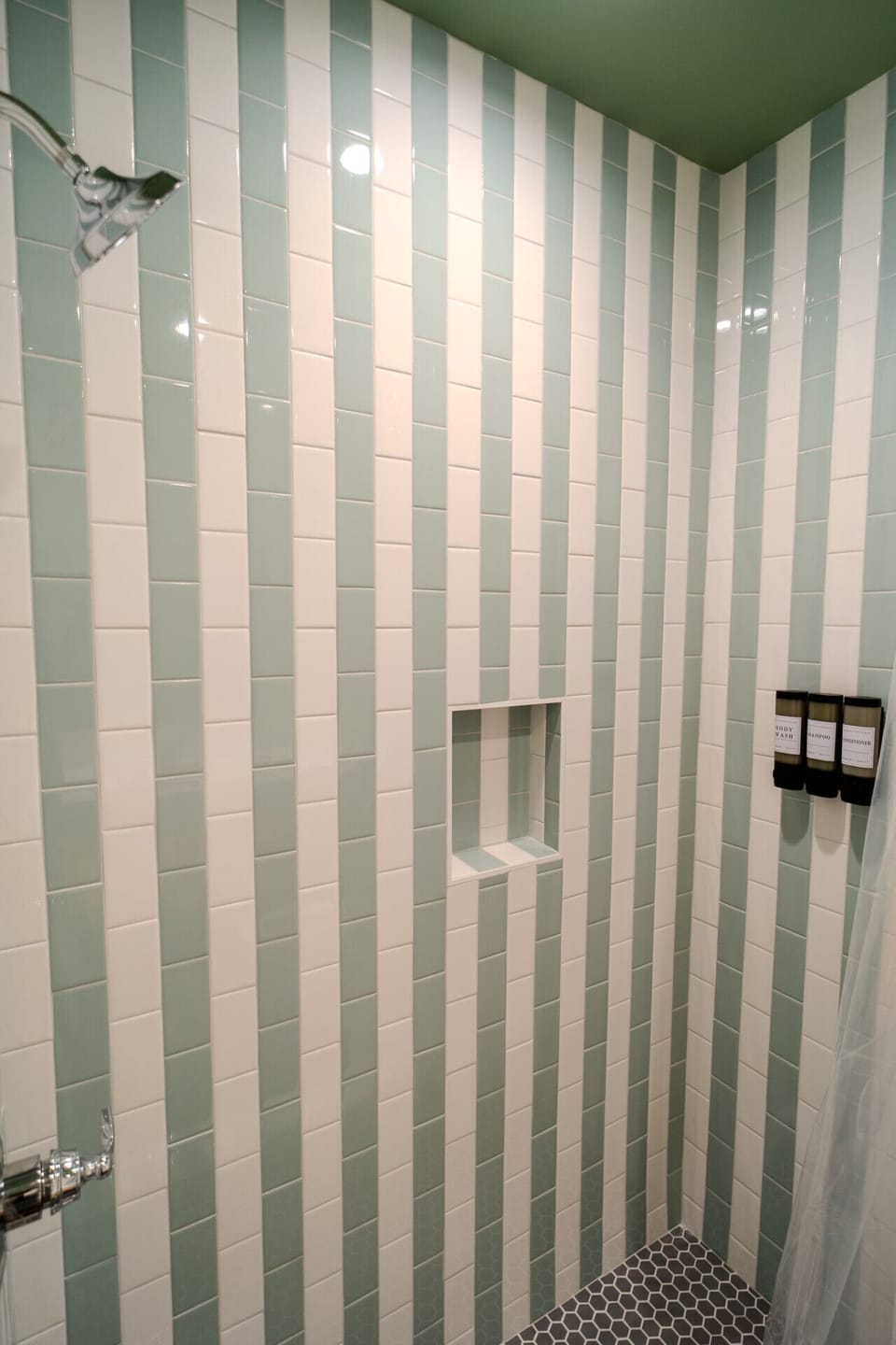 Modern walk-in shower with soft green tile, shampoo and body wash dispensers, and a bright finish