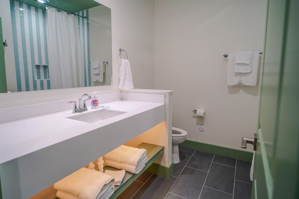 Bright bathroom with a large mirror, soft towels, and walk-in shower with colorful tile