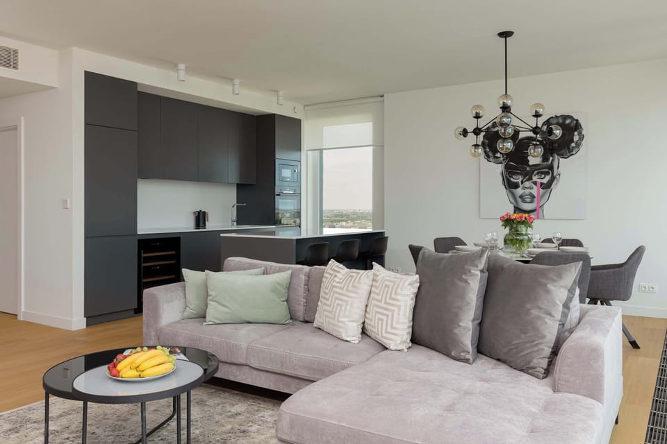 Living room area, focusing on the comfortable gray sofa adorned with patterned cushions. A stylish, minimalist chandelier hangs above, adding to the modern ambiance.