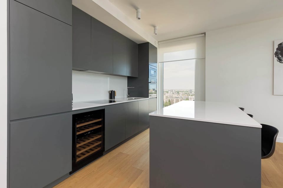 A sleek kitchen with dark cabinetry and light countertops. The setup includes a coffee maker and basic appliances, blending function with style.