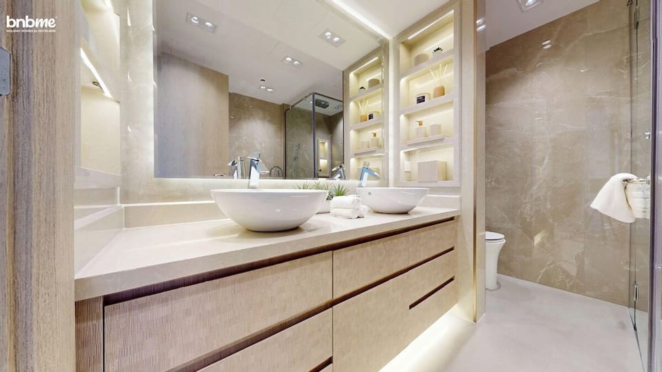 Unwind in the spa-inspired master bathroom featuring a modern freestanding bathtub, rainfall shower, double sinks with stylish vessel basins, sleek vanity storage, and luxury marble finishes—perfect for a relaxing end to your Dubai day.