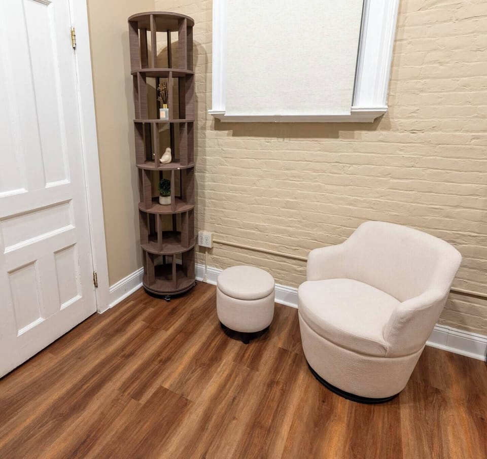 Relax with a book or unwind in the cozy armchair and ottoman, set in a quiet corner with warm tones and stylish shelving accents.