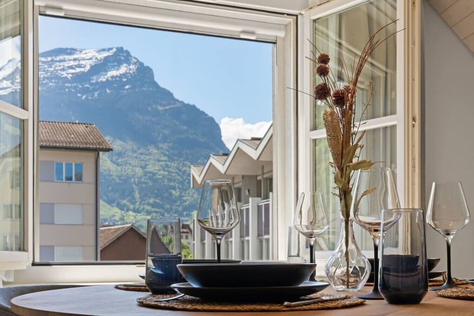 Geniesse eine köstliche Mahlzeit am Esstisch mit Blick auf schneebedeckte Berge und grüne Täler. Der moderne, gemütliche Stil und die weiche Beleuchtung schaffen eine einladende Atmosphäre, die jede Mahlzeit zu einem unvergesslichen Moment macht.
