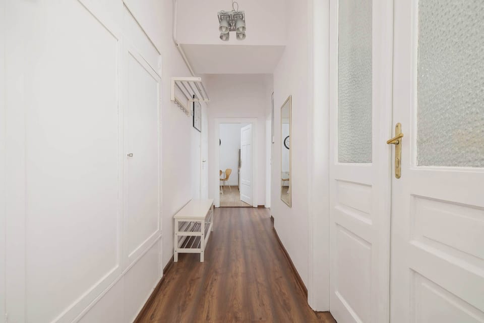 A hallway with bright walls and wooden flooring. White doors lead to different rooms of the apartment.
