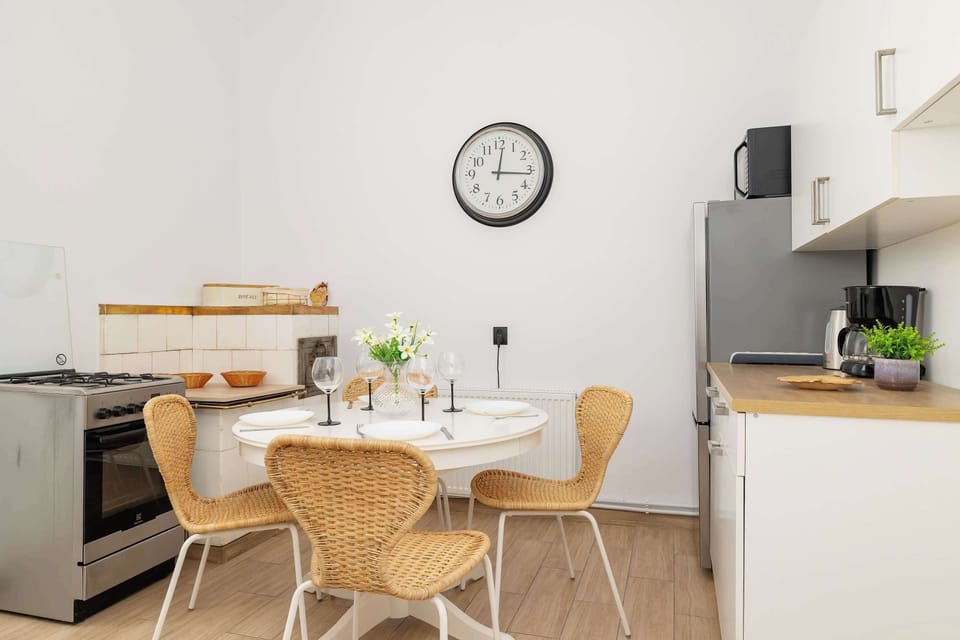 A dining space with a round table, chairs, and wall clock. The kitchen in the background is sleek and functional.