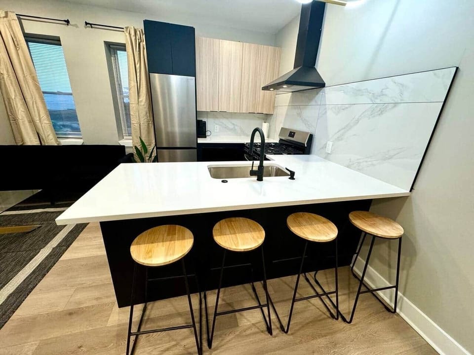 Modern kitchen featuring brand-new appliances, including a breakfast bar, dishwasher, microwave, and refrigerator. It seamlessly connects to the living room, which is furnished with 2 sofa beds, fireplace ,and a flat-screen TV.