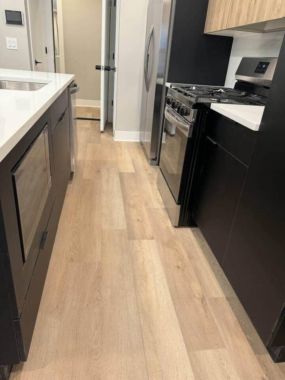 The kitchen counters have been elegantly designed in a sleek black finish. features a large quartz island with barstools. Equipped with appliances, including an oven stove, hood, refrigerator, microwave, dishwasher, and garbage disposal.