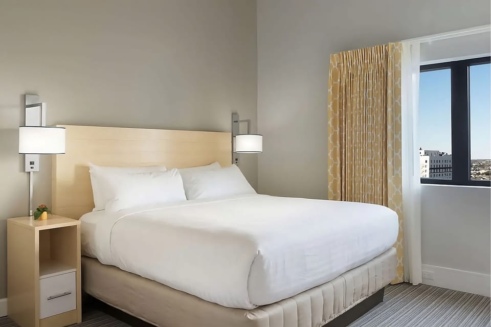 Unwind in crisp linens beside a sunlit city-view window.