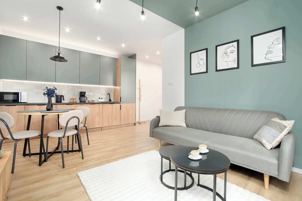 A modern open-plan living and kitchen area, with a sofa and a dining table. Light wood flooring and mint-accented cabinetry create a cozy atmosphere.