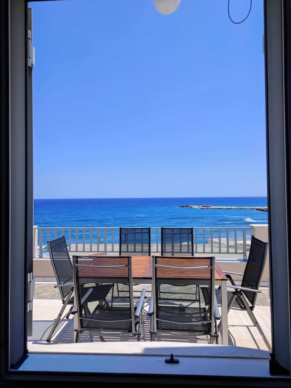Window View of the Terrace and Sea Beyond
Charming snapshot through the window, framing the inviting terrace and the vivid blue waters of the Aegean, emphasizing the property’s privileged location.