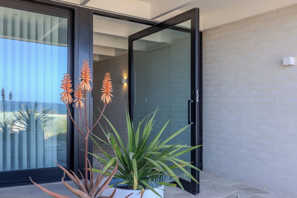 Glass pivot doors at each end of a stone clad hallway. Open for summer breezes.