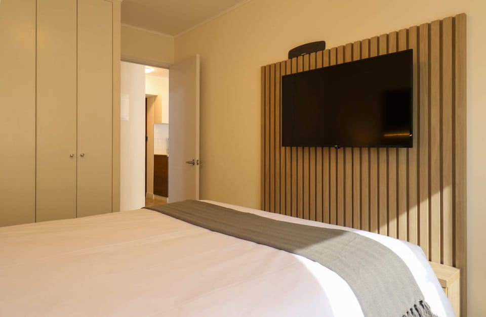 Bedroom with a wall-mounted TV, bed, and closets.