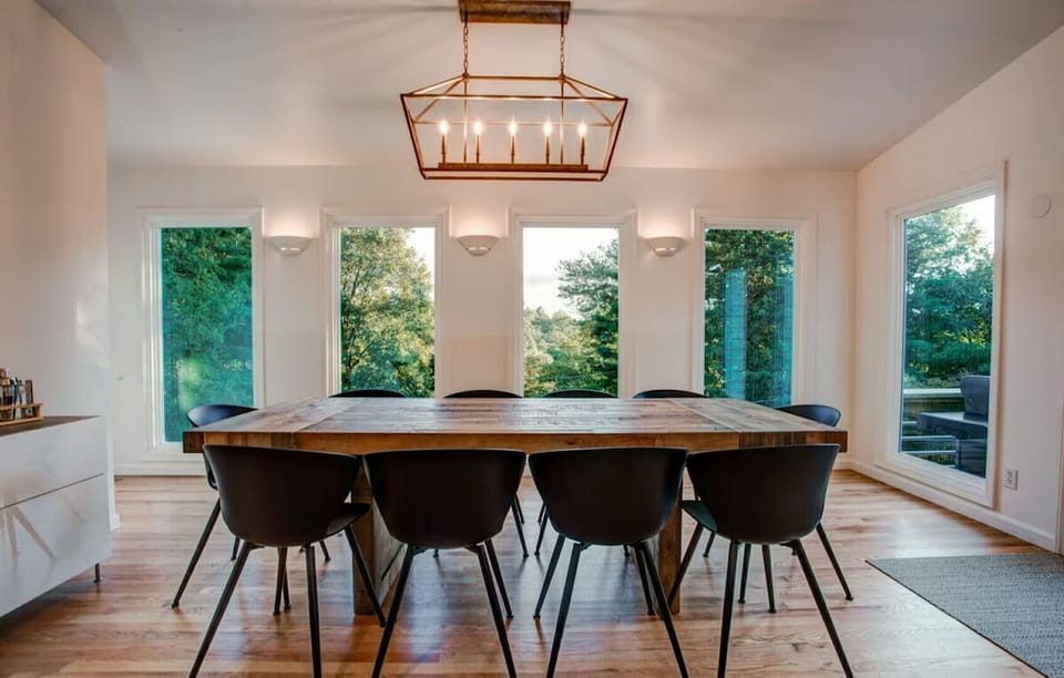 🍽️ Elegant dining area with a reclaimed wood table 🪵, modern black chairs 🪑, and panoramic forest views 🌲—a perfect spot for gatherings and cozy meals 🌅.