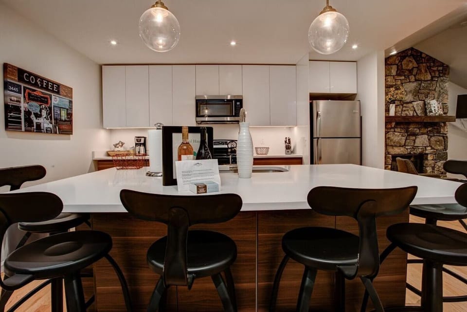 🍷 Sleek modern kitchen with a spacious island 🪑, stainless steel appliances ✨, and warm wood accents—perfect for cooking, coffee ☕, and entertaining by the fireplace 🔥.