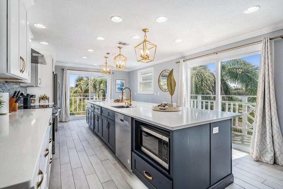 Bright & modern chef’s kitchen with sleek cabinetry, quartz counters, and a grand island with seating. Floor-to-ceiling windows fill the space with natural light and tropical views—perfect for cooking, entertaining & gathering.