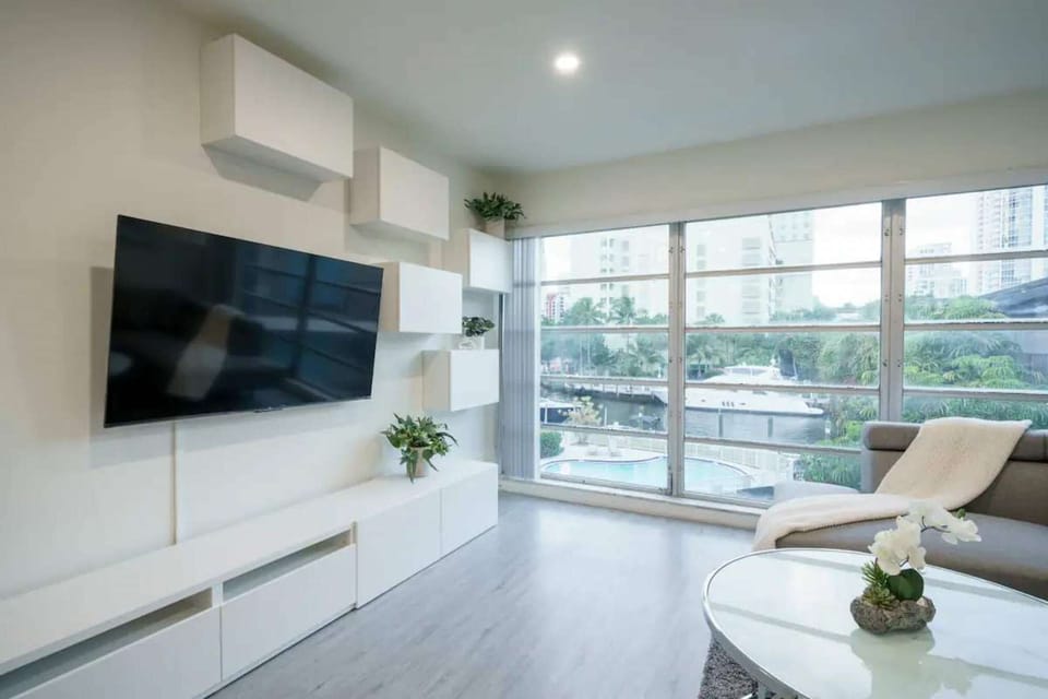 Bright sitting area with wall TV, chair, table, and wide windows