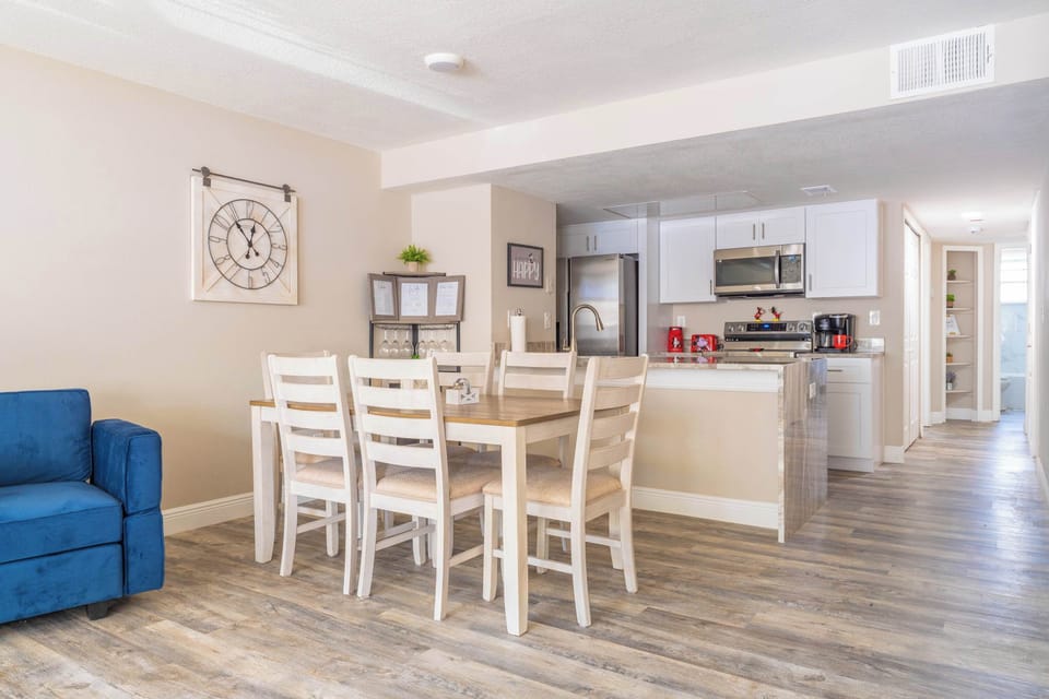 Open dining area with seating for six adjacent to a modern kitchen with stainless steel appliances.