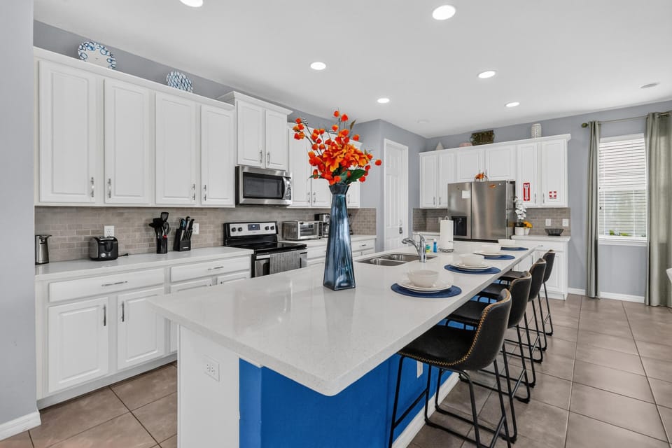Kitchen island with white quartz countertop and black barstools set with white dishes and blue placemats.