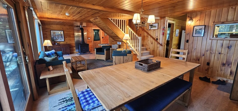 Spacious open-concept dining and living area with rustic wood interiors, cozy wood stove, and comfortable gathering spaces for family and friends.