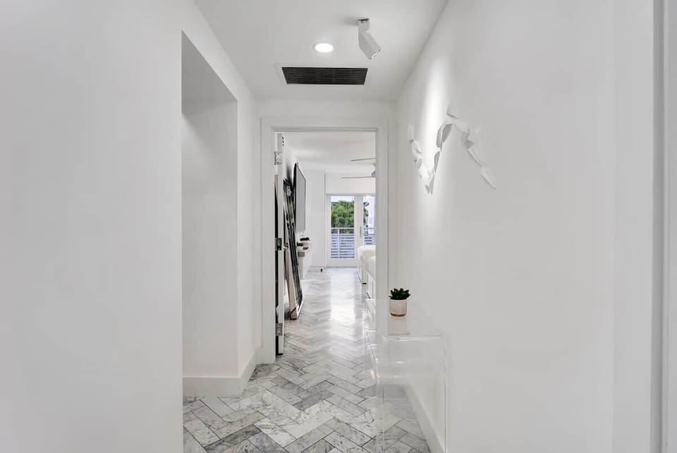 2nd FLOOR: HALLWAY leading from private elevator looking into primary bedroom.  Private bedroom outdoor terrace overlooking Versace Mansion in background.  Wall art.  Italian granite herringbone flooring. 