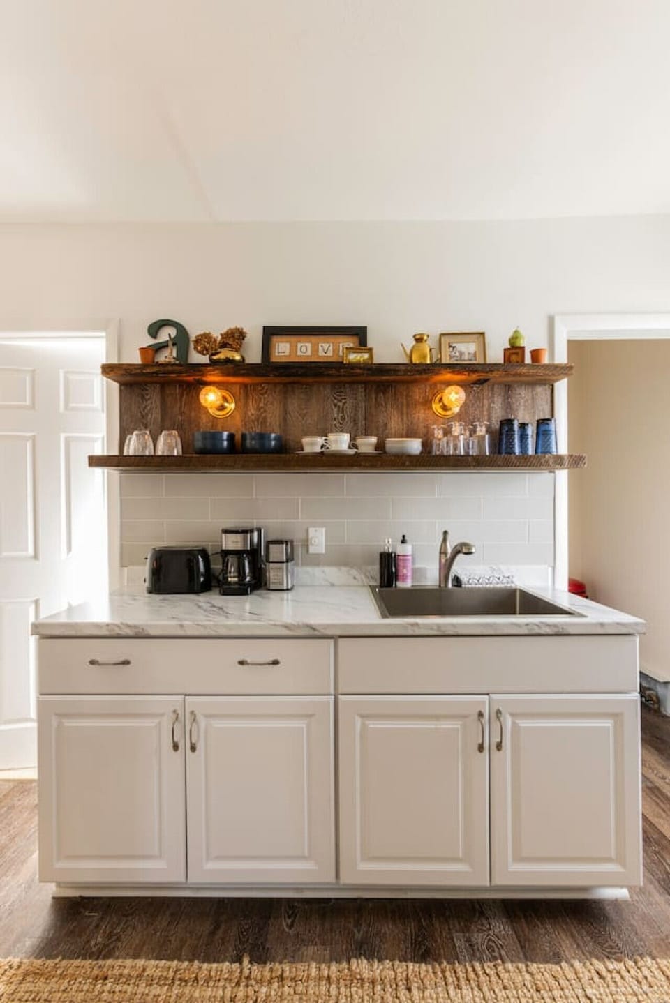Fully equipped kitchen featuring a refrigerator, sink, stove, toaster, coffee maker, salt and pepper, olive oil, microwave, and essential cooking supplies. A bar table seats two, perfect for shared meals. Handcrafted rustic floating shelves, vintage touch
