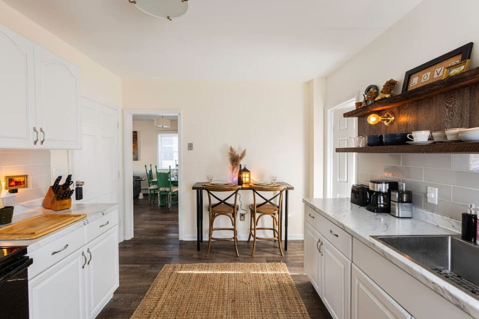 Fully equipped kitchen featuring a refrigerator, sink, stove, toaster, coffee maker, salt and pepper, olive oil, microwave, and essential cooking supplies. A bar table seats two, perfect for shared meals. Handcrafted rustic floating shelves, vintage touch