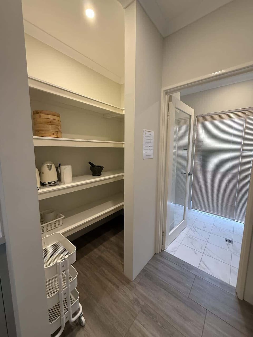This spacious pantry with ample open shelving, a convenient rolling cart, and essential appliances like a toaster and kettle, ensures a comfortable stay. Adjacent, a sleek tiled room with privacy blinds and a glass door awaits.