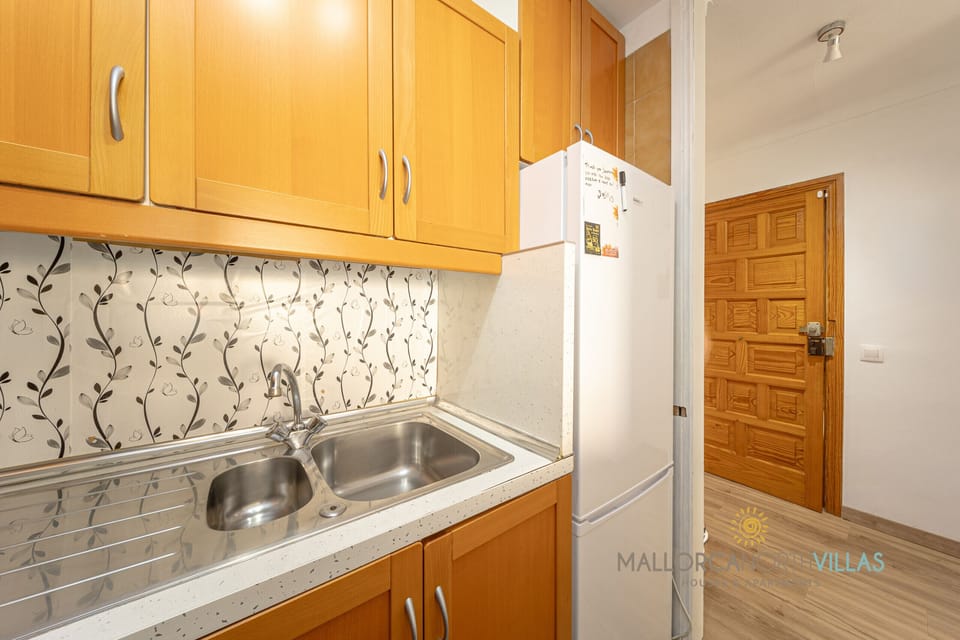 Kitchen sink area with wooden cabinets and fridge in a fully equipped kitchen.