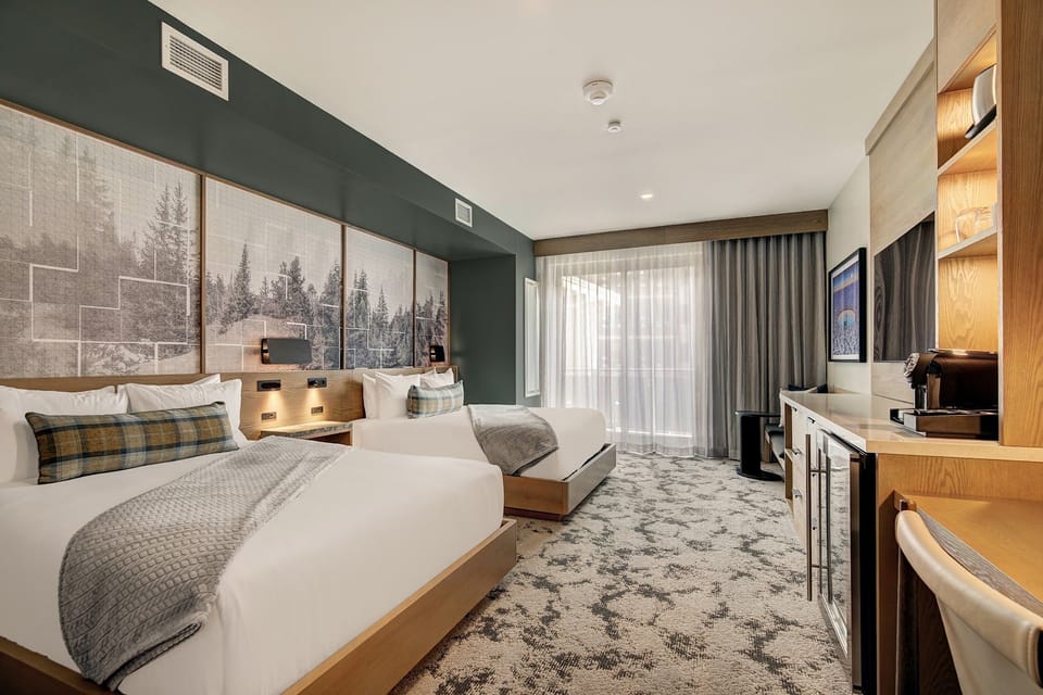 Queen beds with the balcony door ajar and soft bedside lamps — the kind of evening that starts with a view